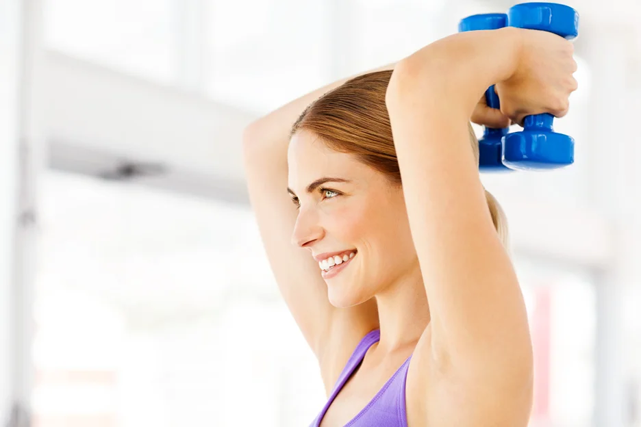 A woman lifting dumbbells to tone and strengthen her arm muscles in a gym.