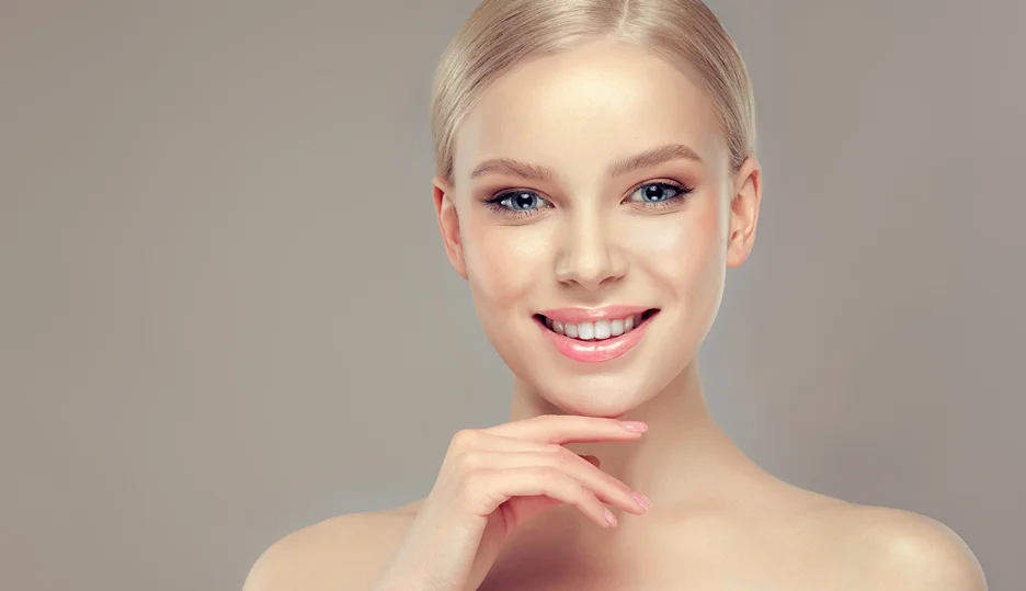 A young woman smiling with her hand on her chin, contemplating the possibility of receiving chin liposuction for a second time.