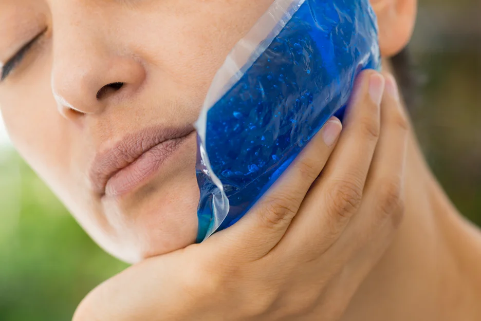 A woman is applying a cold therapy on her chin to minimize swelling after chin liposuction.