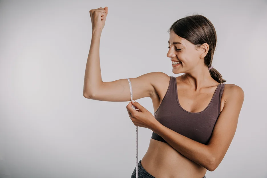 A woman is measuring her arm with a tape measure after getting lipo with j plasma procedure
