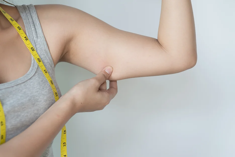 A woman measuring her arm with a measuring tape in preparation for Transaxillary Brachioplasty.