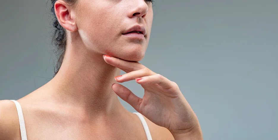 A woman showcasing her slimmer neck, with her hand on her neck.